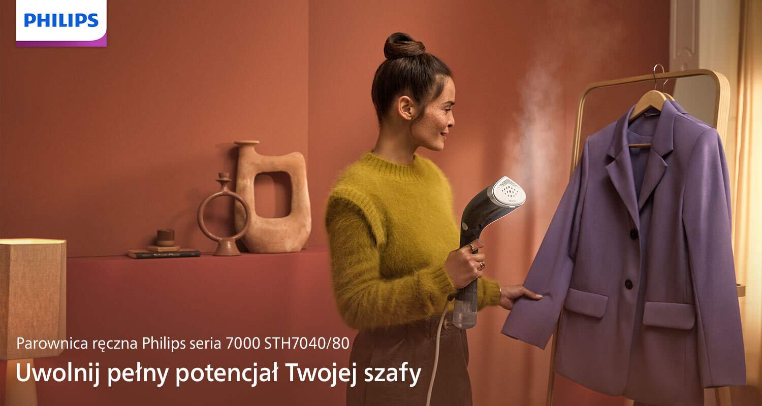 Osoba używa parownicy do ubrań, kierując parę na fioletową marynarkę wiszącą na wieszaku. Widoczny jest tekst: \'Parownica ręczna Philips seria 7000 STH7040/80 Uwolnij pełny potencjał Twojej szafy\'.