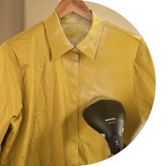 Żółta koszula na wieszaku jest prasowana parownicą do ubrań. Na parownicy widoczne jest logo \'PHILIPS\'.
