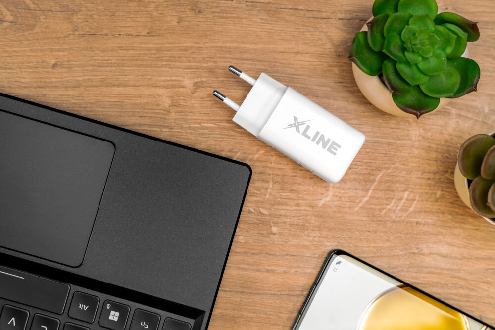 Ładowarka indukcyjna XLINE WCG1003W Biały zabezpieczenia leżąca na blacie obok laptopa smartfona