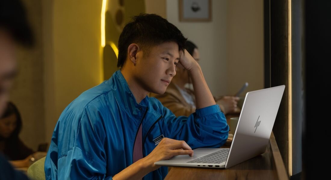 Mężczyzna w niebieskiej koszuli używający laptopa HP OmniBook w nowoczesnym mieszkaniu z żółtym oświetleniem. - Pamięć LPDDR5x   