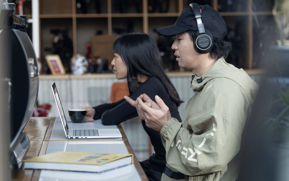 Praca oraz rozmowa przez słuchawki przy laptopie HP OmniBook w kawiarni, obok kobieta pijąca kawę. - Jakość dźwięku DTS:X Ultra HP Audio Boost 