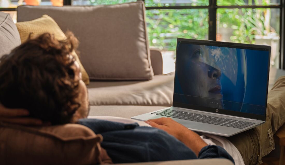 Kobieta oglądająca film na laptopie HP OmniBook leżąc na kanapie z psem w przytulnym salonie - dysk SSD PCIe Gen4 NVMe M.2