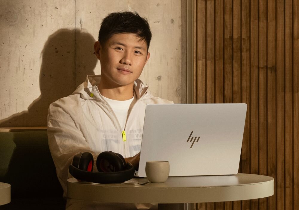 Mężczyzna w białej kurtce pracujący na laptopie HP OmniBook Aero ze słuchawkami przy okrągłym stole. - metale pochodzące z recyklingu        