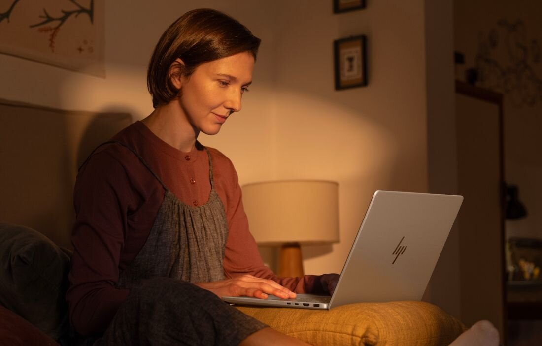 Kobieta w brązowej sukience używająca laptopa HP OmniBook w przytulnym salonie z ciepłym oświetleniem. - dysk SSD PCIe Gen4 NVMe M.2  