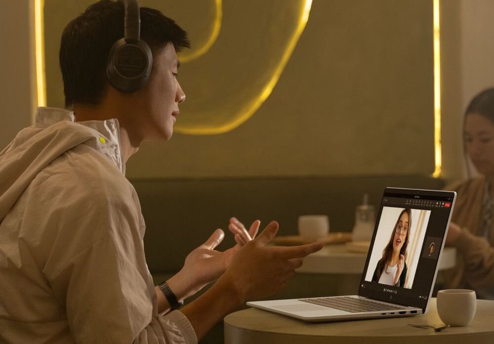 Młody mężczyzna w okularach pracujący na laptopie HP OmniBook w kuchni, podkreślający bezpieczeństwo danych dzięki modułowi TPM i komfort pracy zdalnej. - Fizyczna osłona kamery, Trusted Platform Module 