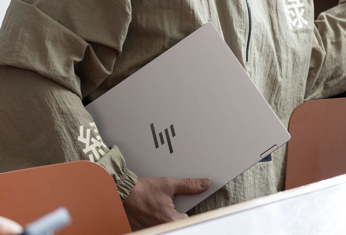 Przenoszenie zamkniętego laptopa HP OmniBook pod ramieniem w nowoczesnym wnętrzu kawiarni. - Bateria o pojemności 68 Wh