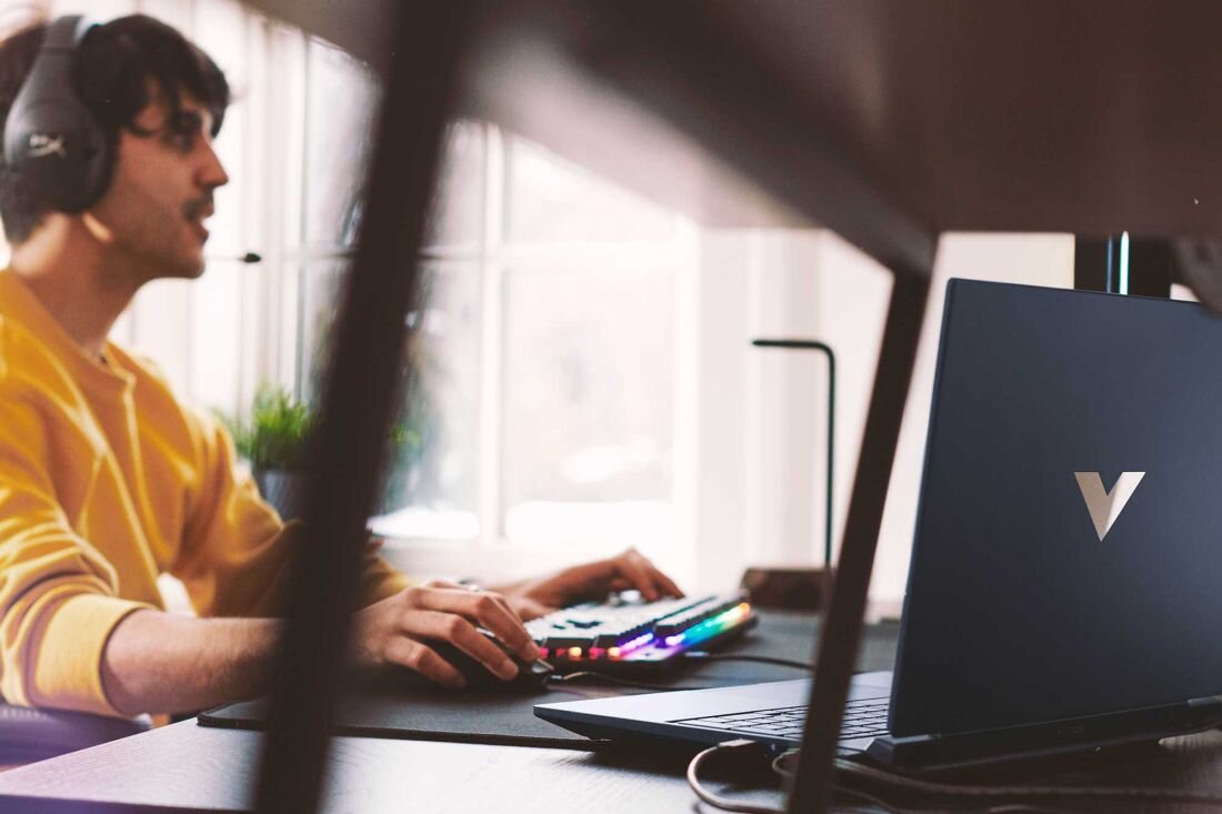 Laptop HP Victus 15 - Mężczyzna w słuchawkach siedzi przy biurku z laptopem, zaangażowany w aktywność związana z technologią. System audio B&O i HP Audio Boost