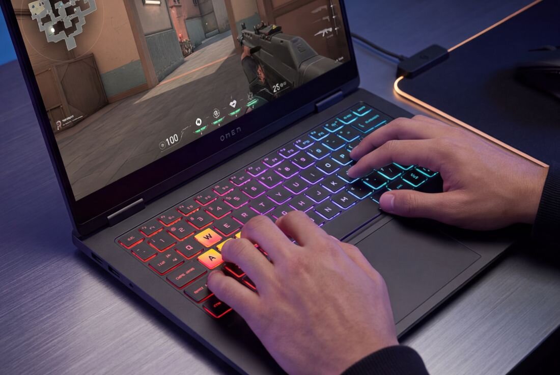 Osoba gra na laptopie HP OMEN Transcend z podświetlaną klawiaturą RGB podczas rozgrywki gamingowej przy biurku  