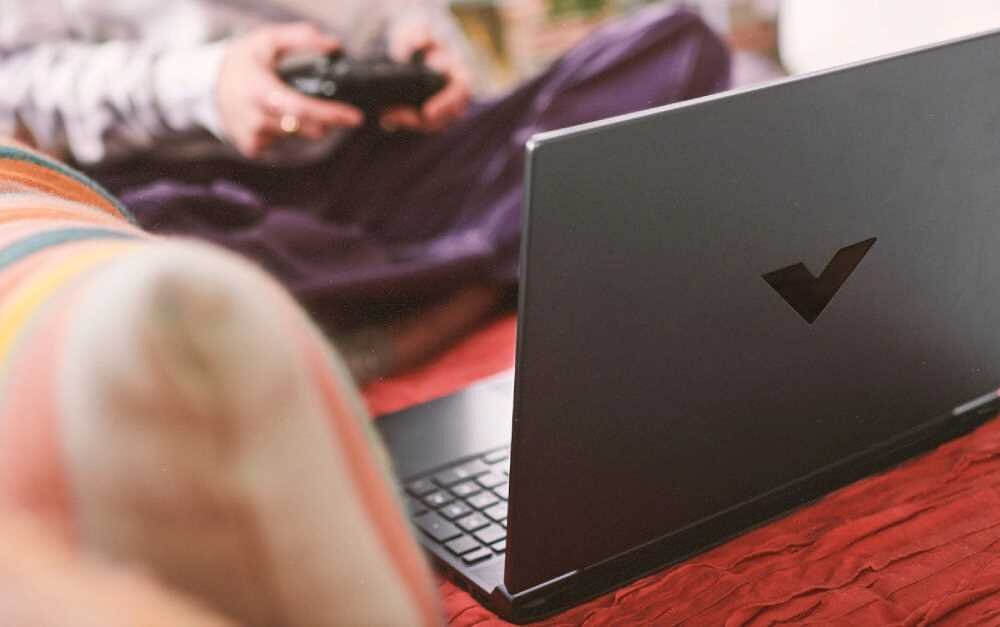 Laptop HP Victus 15 - Osoba grająca w grę wideo na laptopie, skupiona na ekranie, otoczona przyjemną atmosferą. AMD Ryzen, NVIDIA GeForce RTX