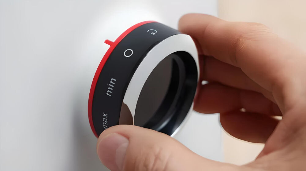 Osoba trzyma pokrętło z oznaczeniami \'min\', \'max\' oraz symbolami graficznymi. Pokrętło ma czerwony i czarny kolor z białymi oznaczeniami.