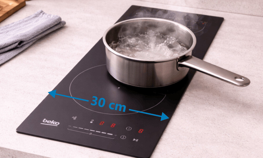Płyta indukcyjna BEKO HDI32400TO Zdjęcie przedstawia płytę indukcyjną Beko z garnkiem z gotującą się wodą oraz zaznaczonym wymiarem 30 cm. Ujęcie podkreśla kompaktową szerokość płyty płyta indukcyjna 30 cm mała kuchnia kompaktowa płyta oszczędność miejsca wymiary 30 x 6 x 52 cm