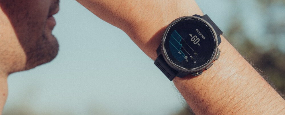 Osoba nosi smartwatch z okrągłym wyświetlaczem, na którym widoczny jest wykres i liczba \'60 m\'.