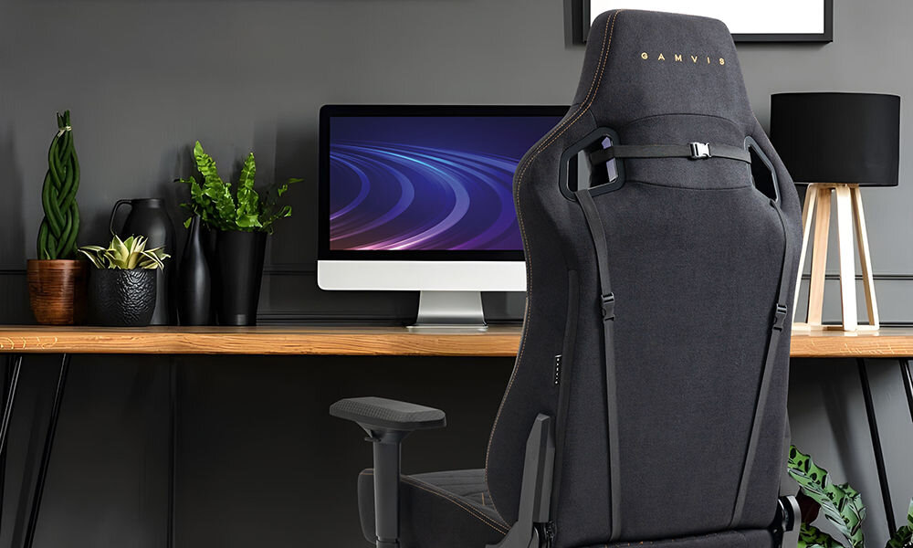 Fotel GAMVIS Elite 2.0 Pro XXL Czarny (złote elementy) prezentacja fotela w pokoju przy biurku na nim monitor obok kwiatki lampka brązowy blat biurka płaskie siedzisko ZeroStress+ mechanizm bujania MultiLockSpec+ wygoda