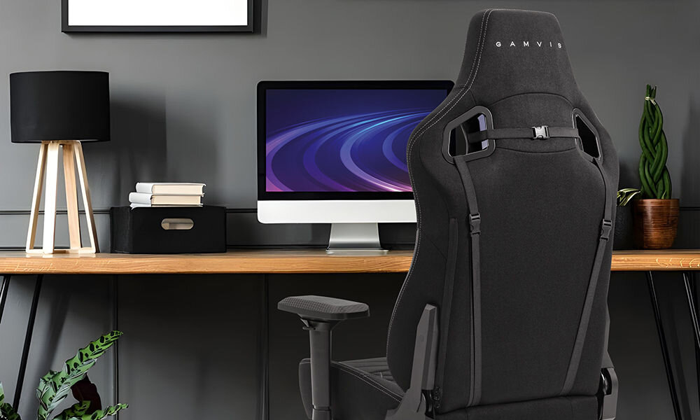 Fotel GAMVIS Elite 2.0 XL Basic Czarny (białe elementy) prezentacja fotela w pokoju przy biurku na nim monitor i akcesoria lampka kwiatek pojemnik z książkami szara ściana płaskie siedzisko ZeroStress+ mechanizm bujania TiltSpec+ wygoda