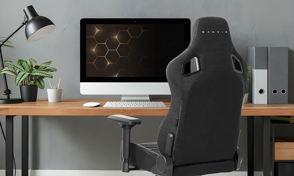 Fotel GAMVIS Elite 2.0 Pro XL Czarny (białe elementy) prezentacja fotela w pokoju przy biurku na nim monitor i akcesoria komputerowe kwiatek lampka brązowy blat biurka detale płaskie siedzisko ZeroStress+ dekoracyjne przeszycia welurowe poduszki wsparcie wygodnej pozycji