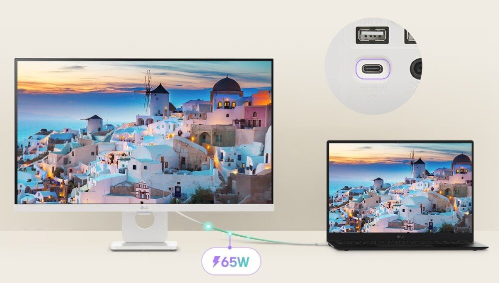 Monitor LG Smart 27U731SA-W.AEU Monitor połączony jednym jasnym kablem z laptopem, gdzie oba ekrany wyświetlają ten sam nadmorski krajobraz z białymi domkami, z widocznym w tle powiększeniem portu USB-C oraz fioletową grafiką informującą o ładowaniu z mocą '65W', porty, Power Delivery, podłączenie