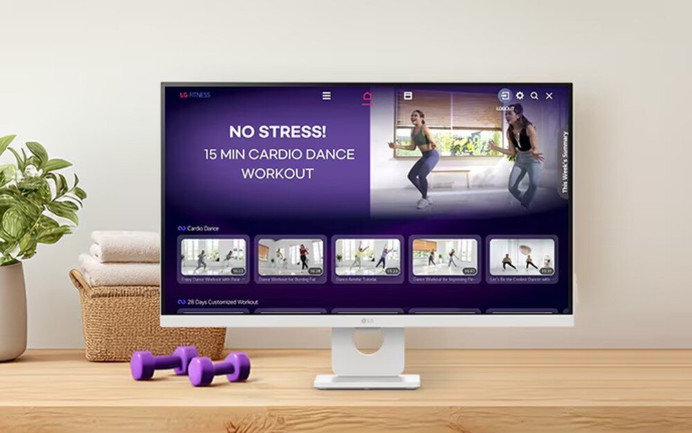 Monitor LG Smart 27U731SA-W.AEU Ekran z włączoną aplikacją LG Fitness wyświetlającą kadr z domowego treningu cardio obok fioletowych hantli leżących na drewnianym blacie, usługi, powłoka matryca