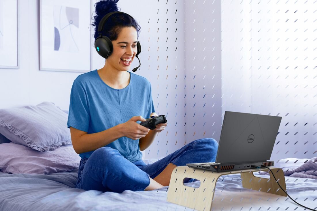 Kobieta na łóżku korzysta z laptopa DELL G15 ma na sobie słuchawki koncentrując się na zadaniu - Stabilny gaming online Wi-Fi 6