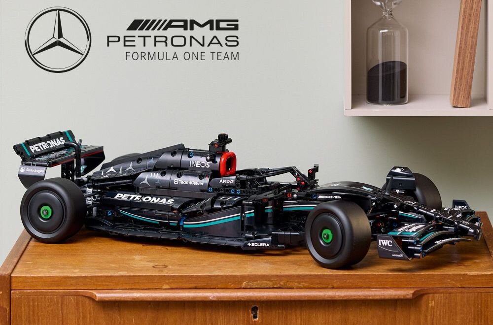 Model samochodu wyścigowego z klocków LEGO, przedstawiający pojazd Formuły 1, stoi na drewnianej powierzchni. Na ścianie widoczne jest logo AMG Petronas Formula One Team.