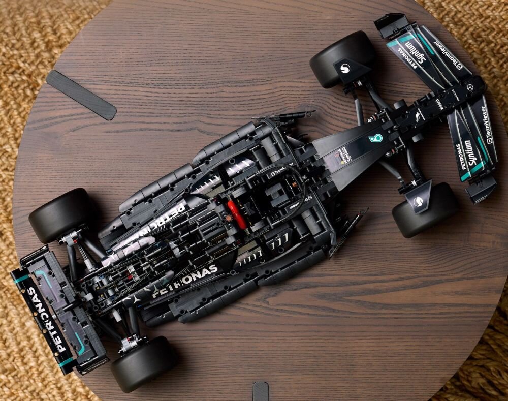 Model samochodu wyścigowego z klocków LEGO, przedstawiający szczegółową konstrukcję z widocznymi napisami \'PETRONAS\', \'Epson\', \'CrowdStrike\', \'Tommy Hilfiger\', \'Pirelli\', \'Petronas Syntium\', \'E Performance\', \'Mercedes\', \'AMG\', \'Petronas Primax\'. Model jest umieszczony na drewnianym stole.