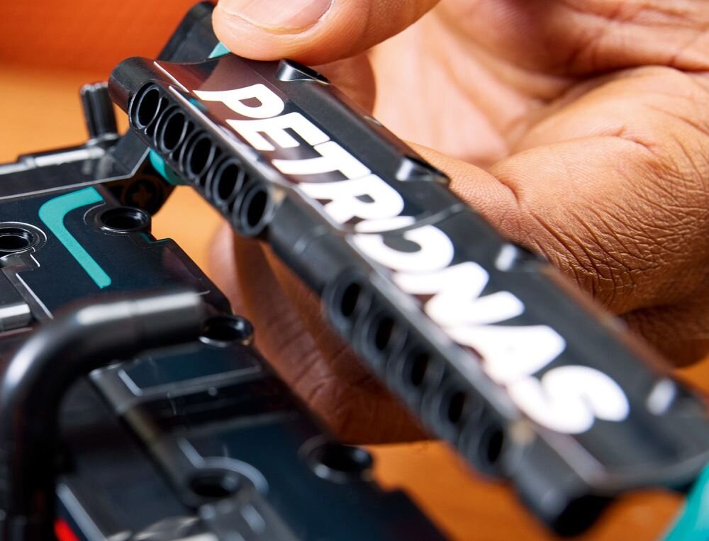 Zbliżenie na rękę trzymającą element konstrukcyjny z napisem \'PETRONAS\'. Element jest częścią zestawu LEGO Technic.