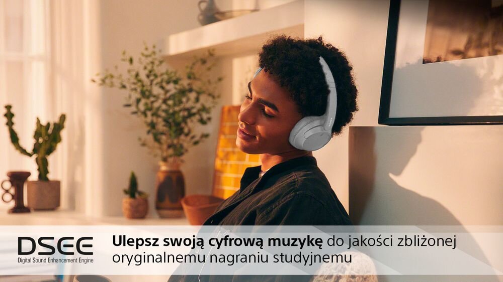 Osoba nosi czarne słuchawki nauszne, siedząc w jasnym pomieszczeniu z roślinami i dekoracjami. Na obrazie widoczny jest tekst: \'DSEE Digital Sound Enhancement Engine Ulepsz swoją cyfrową muzykę do jakości zbliżonej oryginalnemu nagraniu studyjnemu\'.