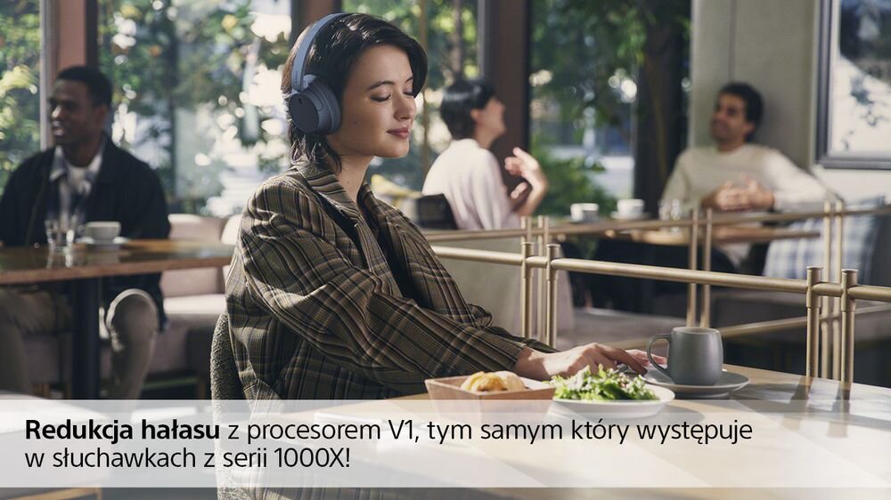 Osoba siedzi przy stole w kawiarni, nosząc czarne słuchawki nauszne. Na dole obrazu widnieje tekst: \'Redukcja hałasu z procesorem V1, tym samym który występuje w słuchawkach z serii 1000X!\'.
