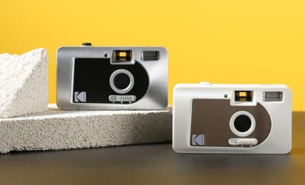 Dwa aparaty analogowe w kolorach srebrnym i białym stoją na jasnym tle. Na obu widoczne jest logo Kodak.