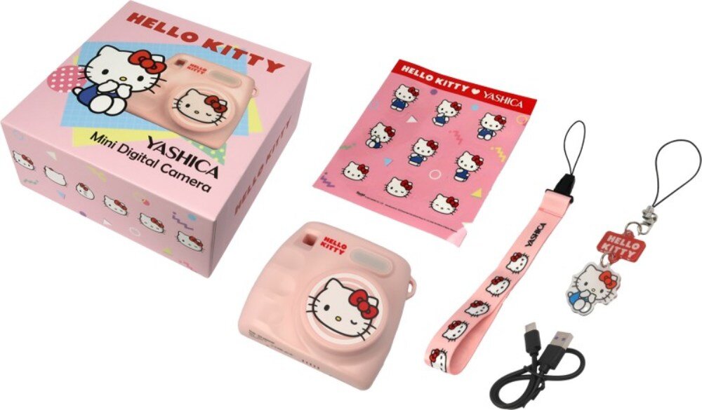 Zestaw zawiera różowy aparat z motywem Hello Kitty, pudełko z napisem \'HELLO KITTY YASHICA Mini Digital Camera\', smycz, brelok oraz kabel USB. Obok znajduje się arkusz z naklejkami przedstawiającymi postać Hello Kitty.