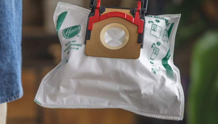 Na zdjęciu widoczny jest worek do odkurzacza z logo \'Hoover\' oraz instrukcjami użytkowania nadrukowanymi na powierzchni. Worek ma otwór z plastikowym uchwytem w kolorze czerwonym i beżowym.