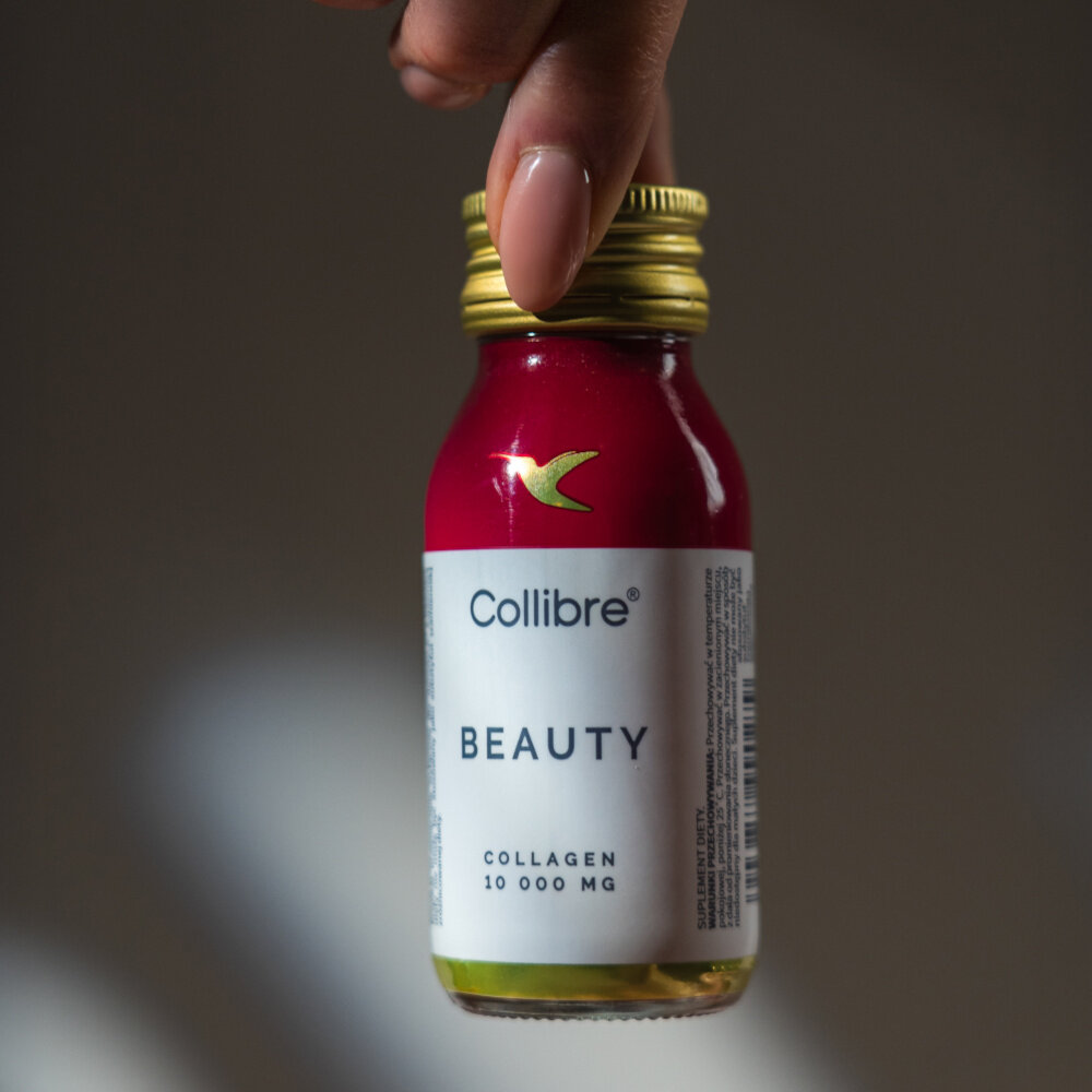 Kolagen COLLIBRE Beauty shot 15 x 60 ml osoba trzyma buteleczkę za nakrętkę 10 000 mg hydrolizatu kolagenu wołowego o małych cząsteczkach 2000 Da duze wchłanianie gładkość jędrność wzbogacony witaminą C 80 mg naturalna synteza kolagenu