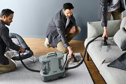 Mężczyzna używa odkurzacza piorącego 2w1 Clean It IZ3020 do czyszczenia plamy na dywanie, kanapie i foteliku dziecka.