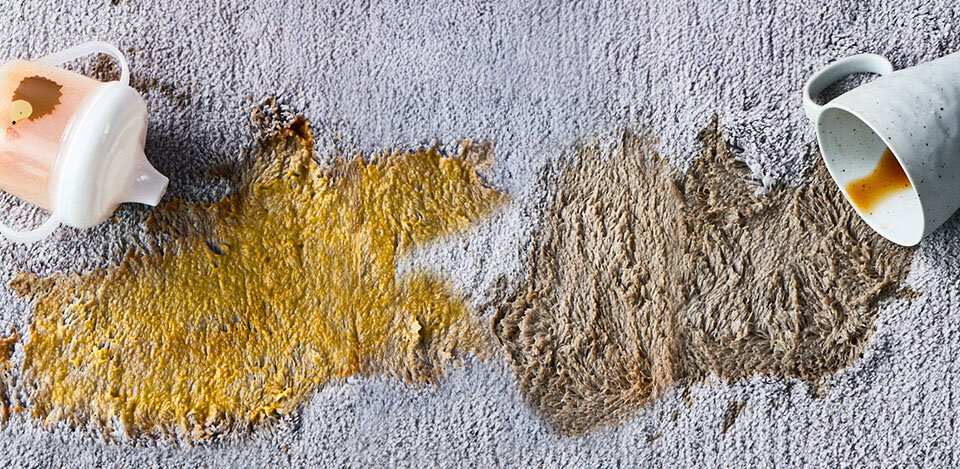 Dwie duże plamy na dywanie - z kawy i soku. Widoczny kubek dla dziecka i kubek z kawą.