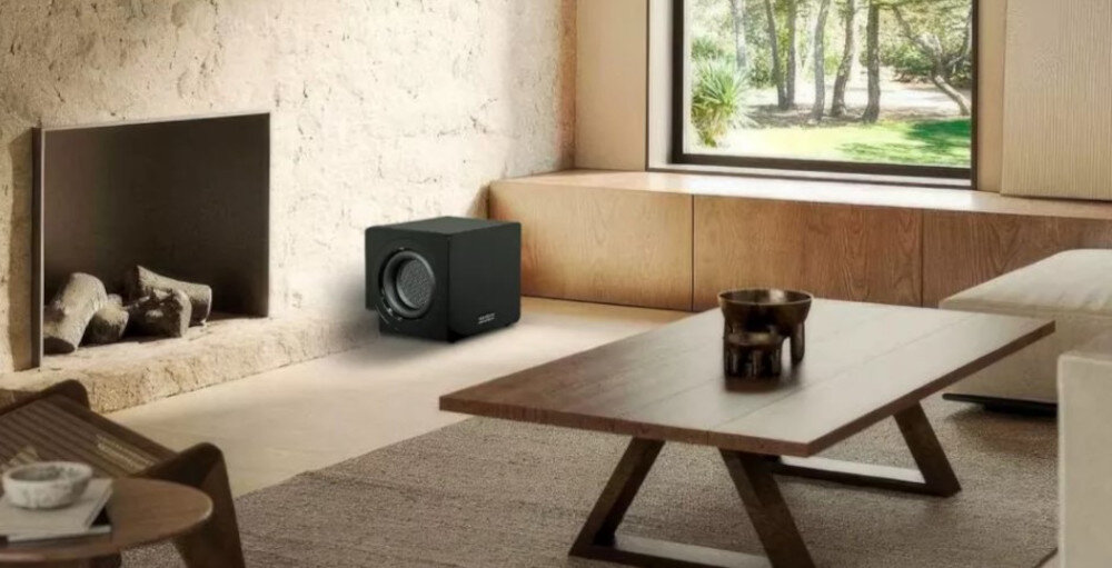 Subwoofer VELODYNE MicroVee X 6.5 moc wyjściowa 800 W, duże magnesy ferrytowe, subwoofer stojący na podłodze w pomieszczeniu obok kominka