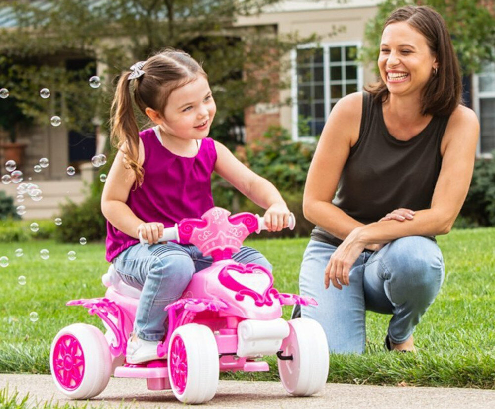 Quad elektryczny dla dziecka HUFFY Princess Bubble 19055W Różowy podwórko trawnik chodnik a quadzie siedzi dziecko za quadem widoczne bańki obok kuca dorosła osoba w tle dom trawnik zabawa frajda bajkowy świat