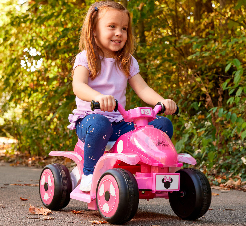 Quad elektryczny dla dziecka HUFFY Minnie Mini 19075W Ciemnoróżowy park dziecko siedzi na pojeździe w tle drzewa komfortowe uchwyty odpowiednio wyprofilowane siedzisko stabilne podnóżki wspierają prawidłową postawę ułatwiają sterowanie