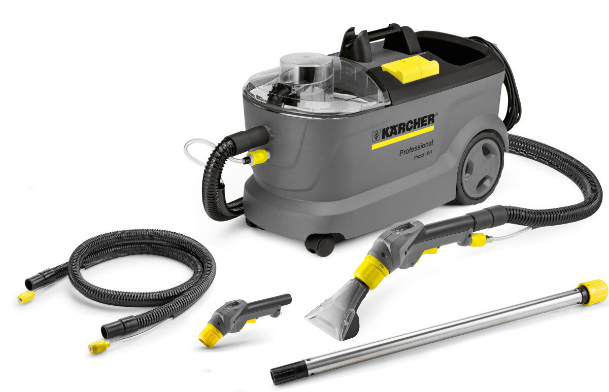 Na obrazie znajduje się urządzenie ekstrakcyjne w kolorze szarym z logo \'KARCHER Professional Puzzi 10/1\'. Wokół urządzenia leżą różne akcesoria, takie jak węże i dysze.