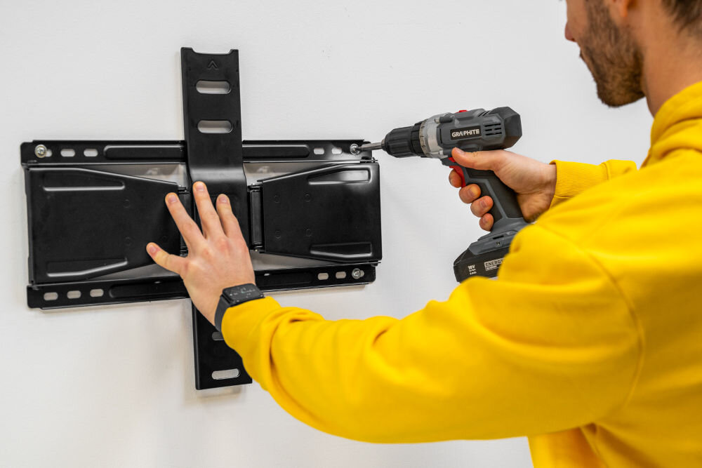 Osoba montująca uchwyt GOLDENLINE do TV 37-90 cali TM3790FMUS do ściany za pomocą wkrętarki