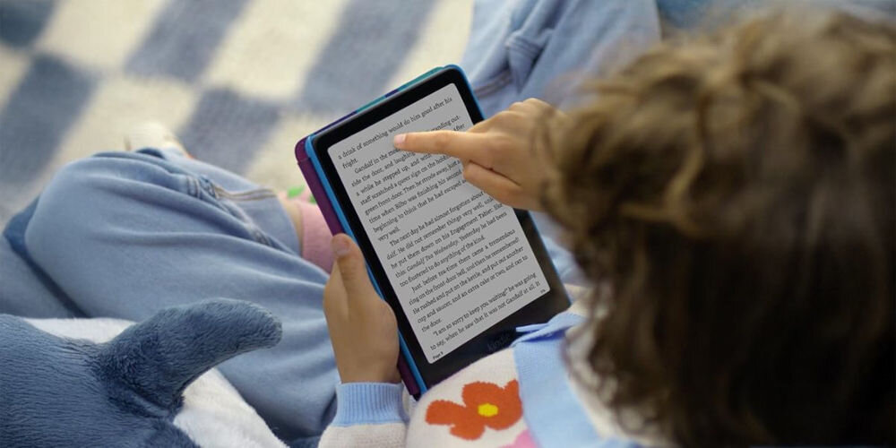 Czytnik e-booków AMAZON Kindle Paperwhite Kids Diary of a Wimpy Kid 7 cali, Podświetlany ekran, Wi-Fi, Bez reklam Dziecko siedzi i dotyka ekranu czytnika Kindle Paperwhite, trzymając go w obu rękach ekran E Ink ostre ilustracje technologia elimunująca odblaski regulowane podświetlenie dostosowanie rozmiaru i grubości czcionki formaty czcionka OpenDyslexic dzieci z dysleksją