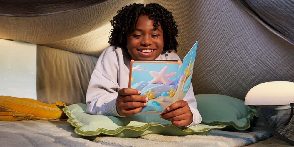 Czytnik e-booków AMAZON Kindle Paperwhite Kids Diary of a Wimpy Kid 7 cali, Podświetlany ekran, Wi-Fi, Bez reklam Dziecko uśmiecha się w namiocie z koców, trzymając Kindle Paperwhite Kids z etui Starfish wytrzymałość baterii złącze USB-C czas ładowania pobór mocy energooszczędny naturalne wrażenia czytelnicze