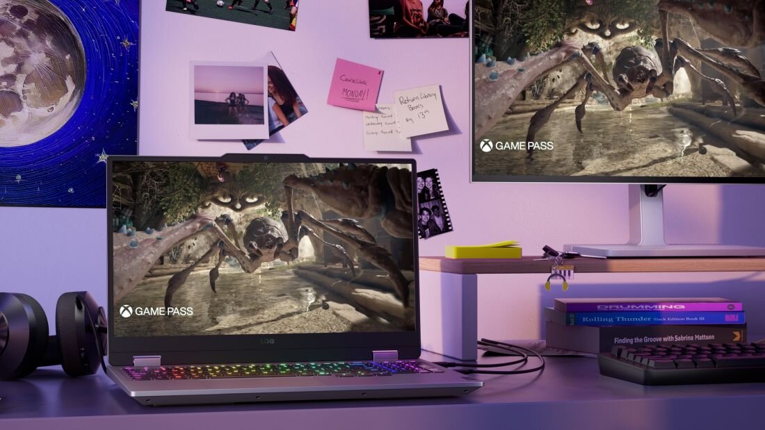 Laptop gamingowy LENOVO LOQ z podświetlaną klawiaturą RGB wyświetlający walkę z potworami przypominającymi owady w prehistorycznej dżungli, logo GAME PASS na ekranie i zewnętrznym monitorze, stonowane fioletowe oświetlenie ambientowe na stanowisku gracza z książkami DRUMMING i Rolling Thunder Black Edition Book III, słuchawki czarne po lewej stronie, klawiatura mechaniczna compactowa po prawej, urządzenie dla graczy korzystających z Xbox Game Pass