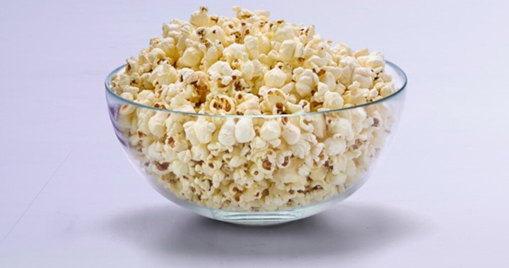 Szklana miska wypełniona popcornem na jasnym tle.