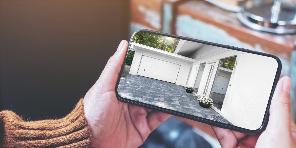 Osoba trzyma smartfon z widokiem na dom i podjazd z kamery zewnętrznej.