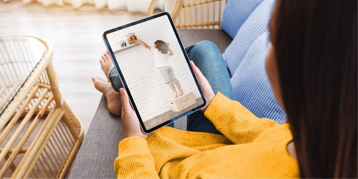 Kobieta oglądająca obraz z kamery (dziecko sięga po ciastka) na tablecie.