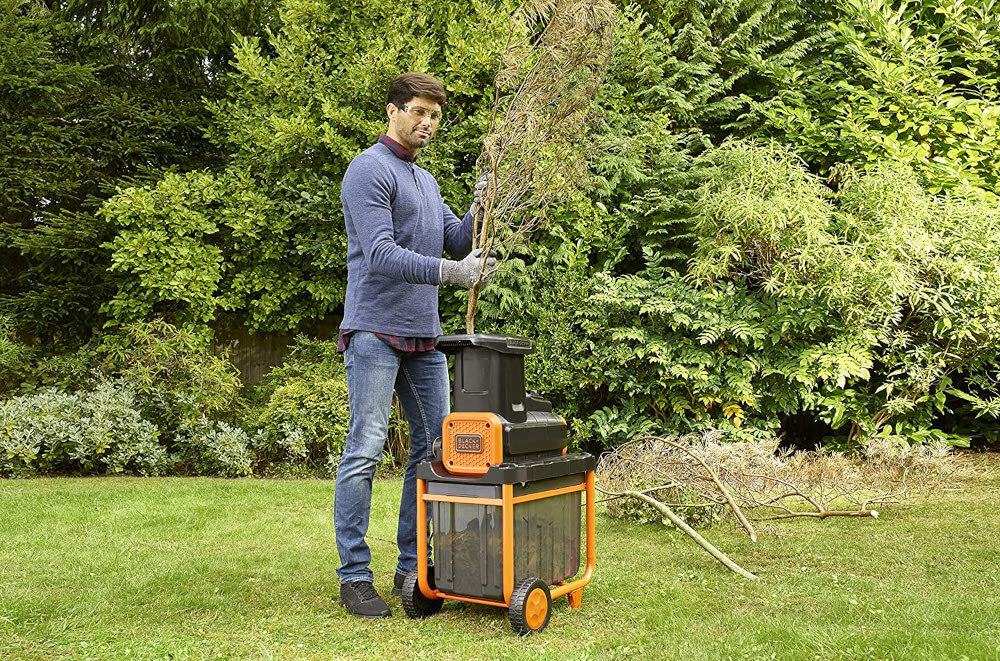 Rozdrabniacz do gałęzi BLACK&DECKER BEGAS5800-QS 2800W 40mm ogród trawnik osoba upycha gałęzie w rozdrabniaczu w tle drzewa krzewy porządek rozdrabnianie odpadków moc wydajność mobilność