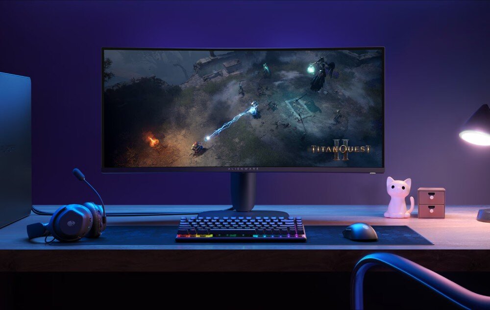 Monitor DELL Alienware AW3425DWM Stanowisko gracza wyposażone w szeroki monitor wyświetlający grę, podświetlaną klawiaturę, mysz, słuchawki oraz ozdobną figurkę kota na drewnianym biurku