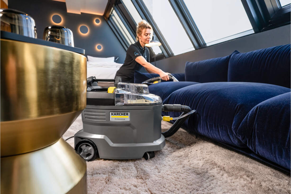 Osoba używa urządzenia ekstrakcyjnego KARCHER do czyszczenia niebieskiej kanapy. Na urządzeniu widoczne jest logo \'KARCHER\'.