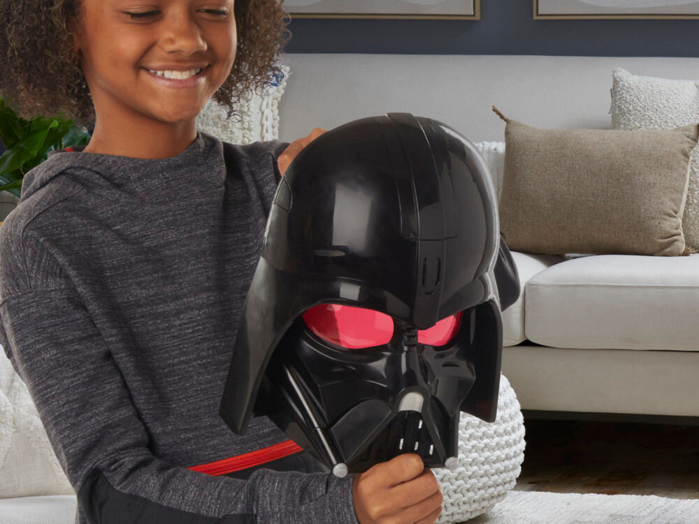 Maska HASBRO Star Wars Darth Vader F94985E0 Zbliżenie na boczny panel maski Hasbro, gdzie palec naciska srebrny przycisk. Ilustracja pokazuje łatwy dostęp do funkcji zmiany głosu i efektów dźwiękowych znanych z Gwiezdnych Wojen.