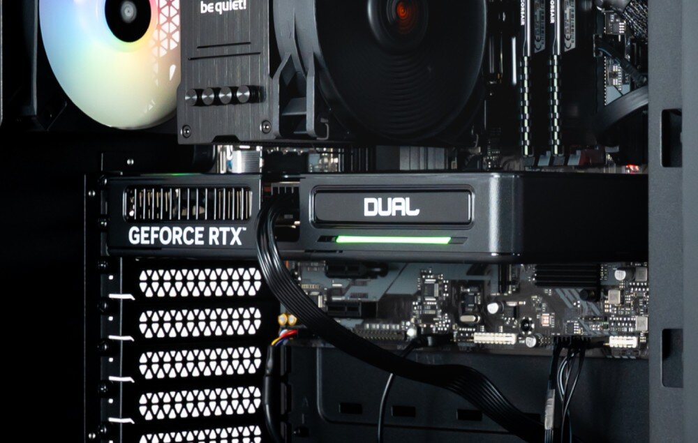 Komputer OPTIMUS E-Sport GB760T-CR16 Wnętrze czarnej obudowy komputerowej, karta graficzna z napisem DUAL i 'GEFORCE RTX' z włączonym podświetleniem ARGB, z boku, karta graficzna, wyjścia wideo