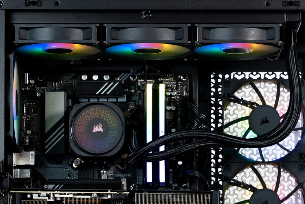 Komputer OPTIMUS E-Sport GB760T-CR17 Widok na górną część wnętrza komputera z trzema podświetlonymi wentylatorami chłodzenia wodnego, procesorem z logo pirata oraz świecącymi kośćmi pamięci RAM, chłodzenie wodne, płyta główna, zasilacz